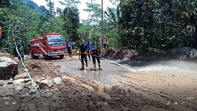 Petugas Damkar Conggeang menyeprot jalan yang masih tertutup lumpur agar dapat segera dilalui kendaraan, Minggu (28/3/2021). (Foto: Fajarnusantara.com)